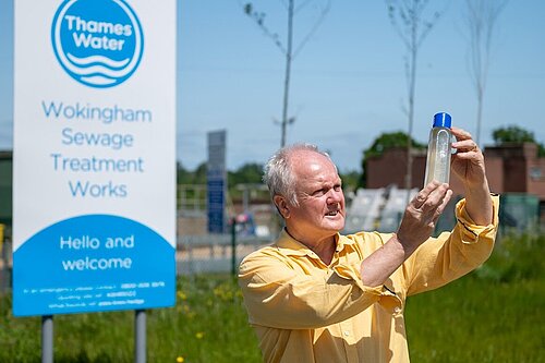 Clive Jones MP stood outside of Thames Water Sewage Treatment Works, inspecting a glass bottle containing polluted river water.