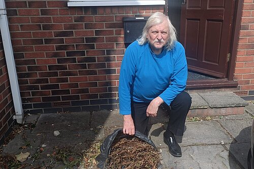 Councillor Tony Fisher kneeling by a bag of garden waste which was dumped at his home