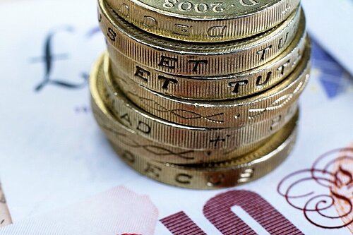 Seven pound coins on top of a ten pound note.